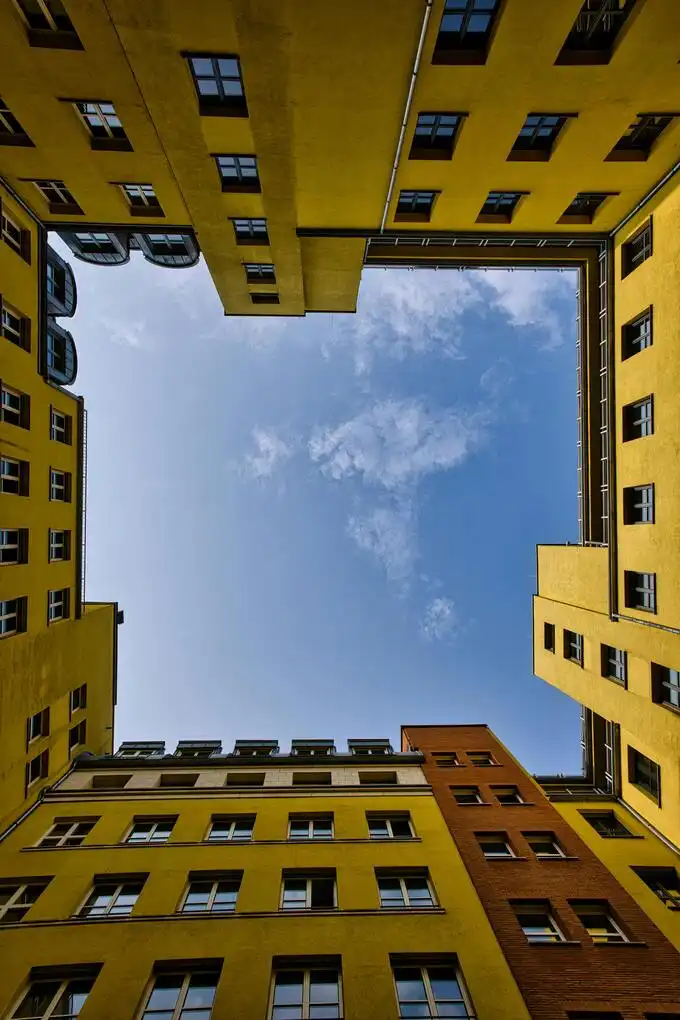 Blick aus einem klassischen Berliner Altbau-Innenhof in Tempelhof mit gelben Fassaden nach oben in den strahlend blauen Himmel, perfekt für Umzüge in Schöneberg & Tempelhof.