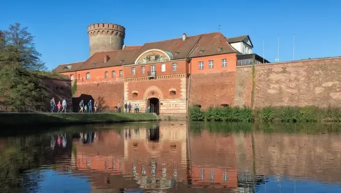 Blick auf die Zitadelle Spandau mit belebter Brücke und Wasserfall-Spiegelung – Ihr Partner für Umzüge im Westen Berlins.
