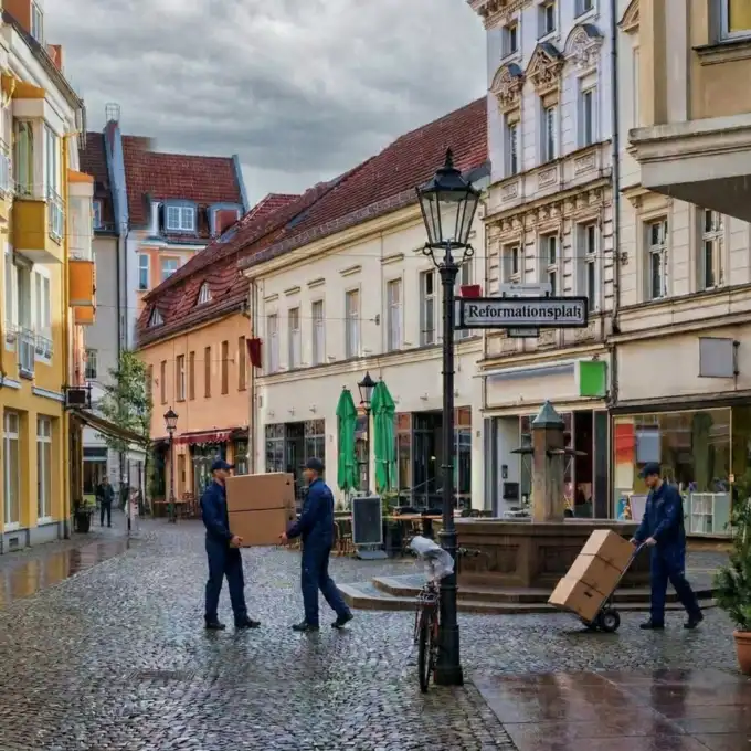 Professionelle Umzugshelfer von Berlinumzugpro beim Transport von Umzugskartons auf dem Reformationsplatz in der Spandauer Altstadt bei Regenwetter.