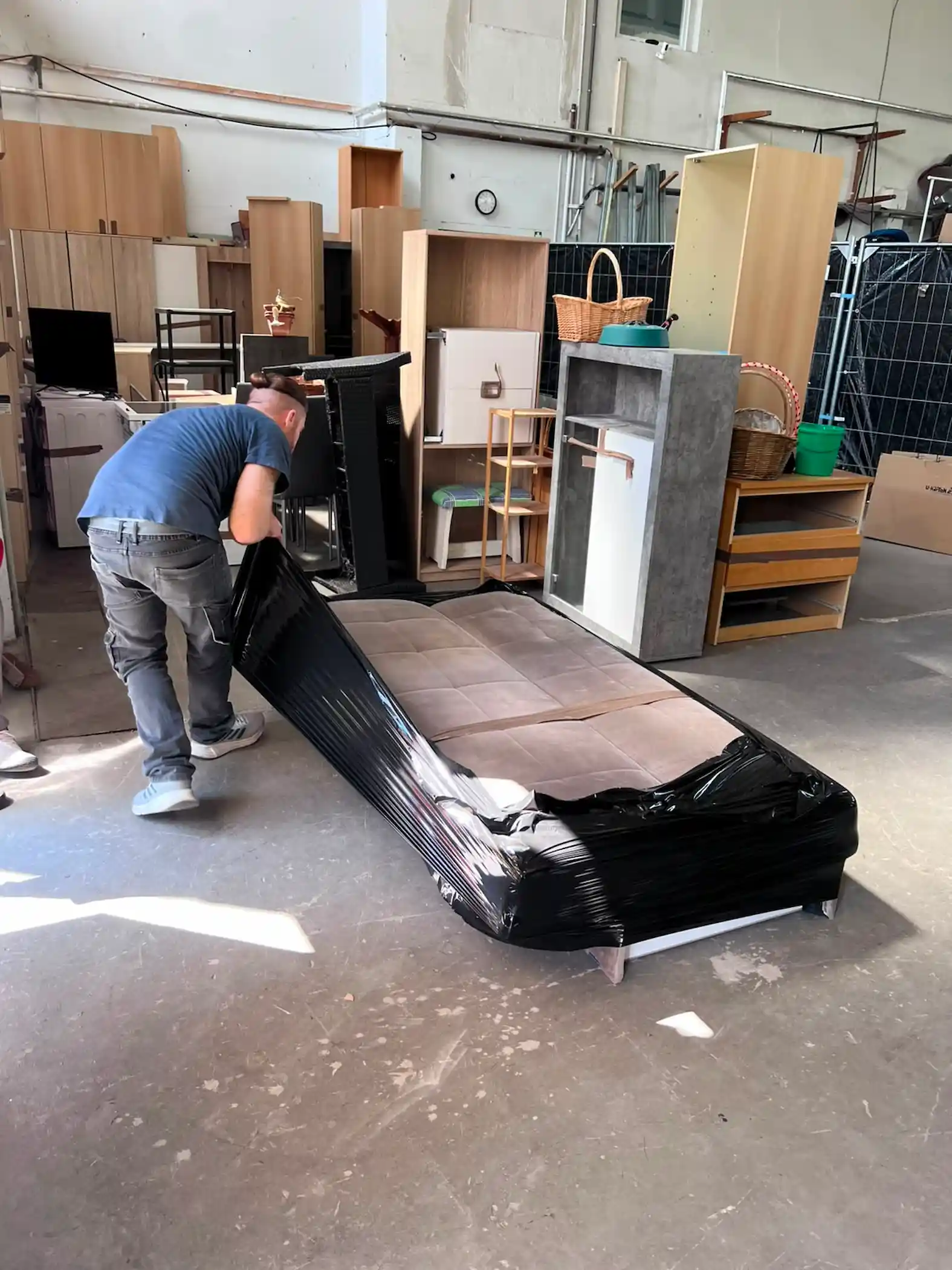 Umzugshelfer verpackt ein Möbelstück mit Decke und Folie für den Transport